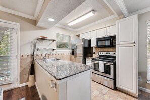 A kitchen with white cabinets, a granite countertop, a stainless steel refrigerator, a microwave, an oven, and a built-in dishwasher.