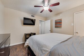 A bedroom with a bed, a ceiling fan, a TV mounted on the wall, and a door.