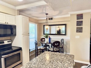 A kitchen with a granite countertop, a built-in microwave, an oven, and a dining area with a table and chairs.