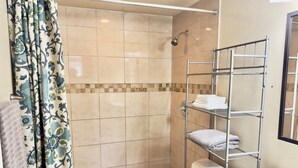 Un baño con ducha, paredes de azulejos, un toallero de metal y un inodoro.