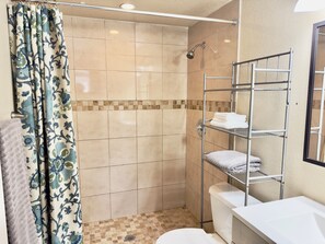 A bathroom with a shower, tiled walls, a metal towel rack, and a toilet.