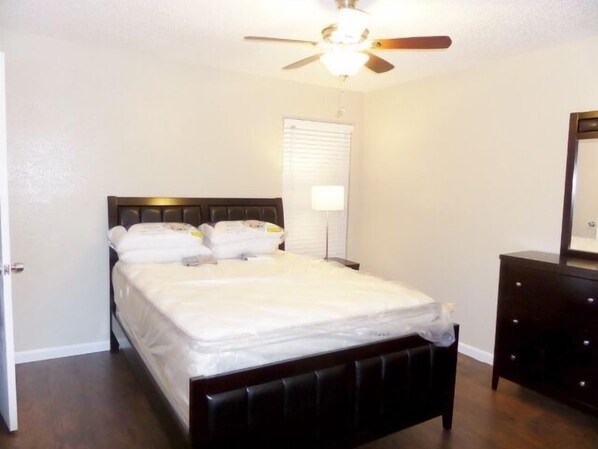 A bedroom with a bed, a nightstand, a dresser, a ceiling fan, and a window with blinds.
