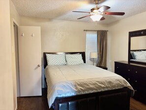 A bedroom with a bed, a ceiling fan, a window with blinds, a nightstand, and a dresser.