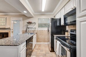 A kitchen with white cabinets, a granite countertop, a black refrigerator, and a stove.