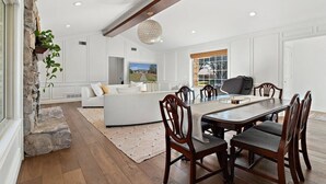 Un vaste espace de vie comprenant une table à manger, des canapés blancs et un mur décoratif en pierre.