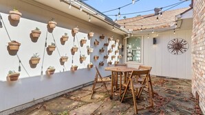 Un espace patio avec une table et des chaises en bois, entouré de jardinières suspendues sur un mur blanc.