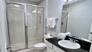 A modern bathroom with a glass-enclosed shower, a white toilet, a sink with a black countertop, and a large mirror.