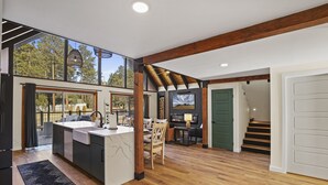 Une cuisine spacieuse dotée d’un grand îlot central, de poutres en bois et offrant une vue sur l’extérieur.