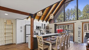 Une cuisine moderne dotée d’un grand îlot central, de poutres en bois et offrant une vue sur la forêt.