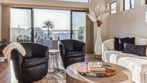 Un salon moderne doté d’une grande fenêtre, de deux fauteuils en cuir noir, d’un canapé blanc et d’une table basse sur laquelle sont posés des livres.