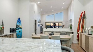 Une cuisine moderne dotée d’un grand îlot central, d’un coin repas avec une table en marbre et de planches de surf accrochées aux murs.