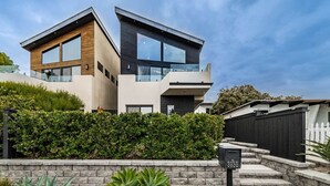 Une maison moderne à deux étages, dotée d’un mur de soutènement en pierre, d’une boîte aux lettres et d’un jardin bien entretenu.