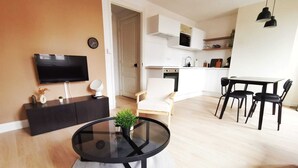 A modern living room with a round glass table, a TV, and a sofa. - Le Contemporain (Lens)