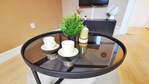 A round glass table with two white cups and saucers, a small plant, and a bottle. - Le Contemporain (Lens)