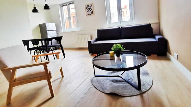 A modern living room with a sofa, a dining table with chairs, a coffee table, and pendant lights. - Le Contemporain (Lens)