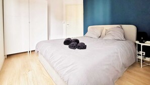 A bedroom with a large bed, a wardrobe, a nightstand, and a ceiling light. - Le Contemporain (Lens)