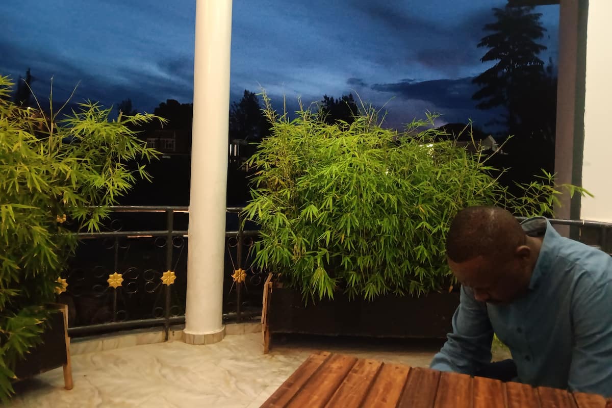 A man sitting at a wooden table in a room with a large column, surrounded by bamboo plants and a mural of a night sky.