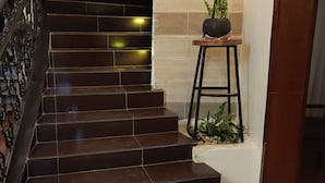 A staircase with dark brown tiles, a metal railing, and a small potted plant on a stool. - La Cafecito Bistro and accommodation  (Kigali)