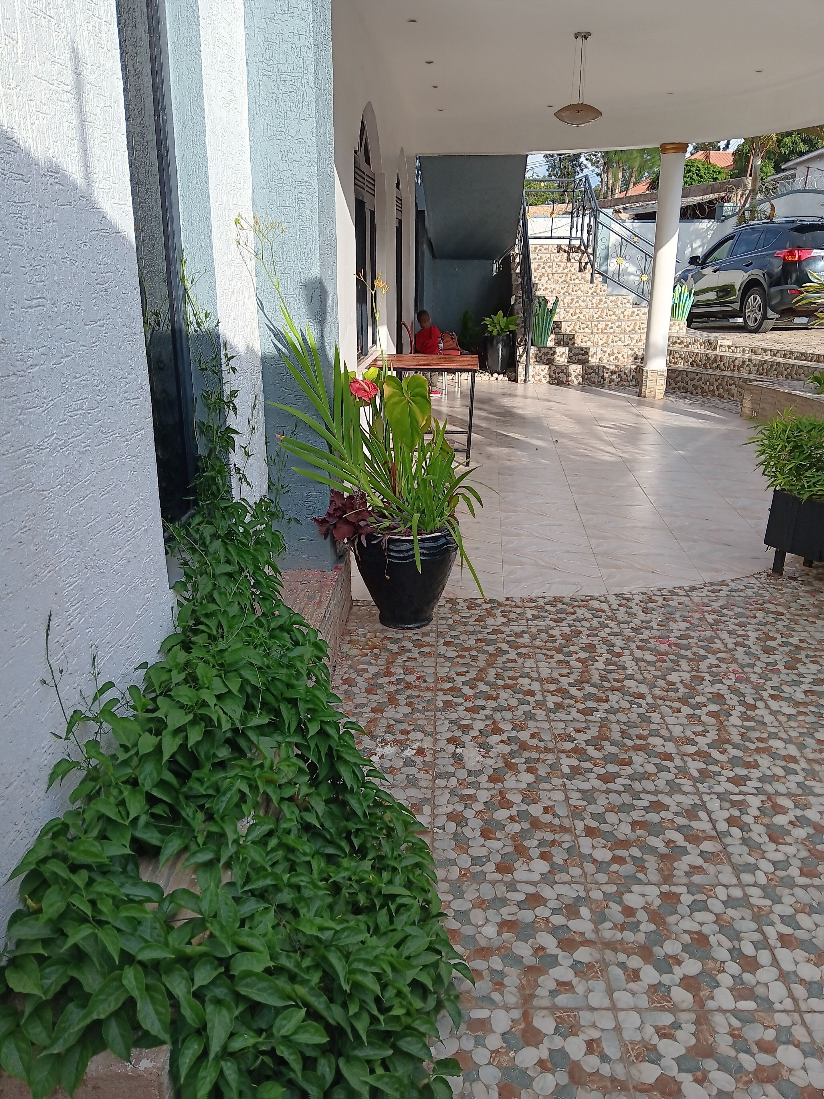 A covered outdoor area with tiled flooring, potted plants, and a staircase leading to an upper level.