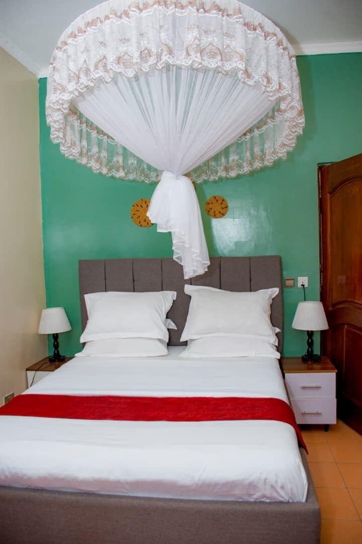 Una cama con dosel blanco, dos mesitas de noche con lámparas, una puerta de madera y una pared verde con dos relojes.