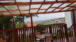 An outdoor wooden deck with a pergola, seating area, and a view of a town and mountains in the distance. - La Cafecito Bistro and accommodation  (Kigali)