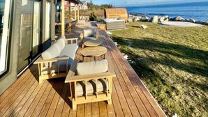 Une terrasse en bois avec des sièges extérieurs, donnant sur une étendue d’eau.