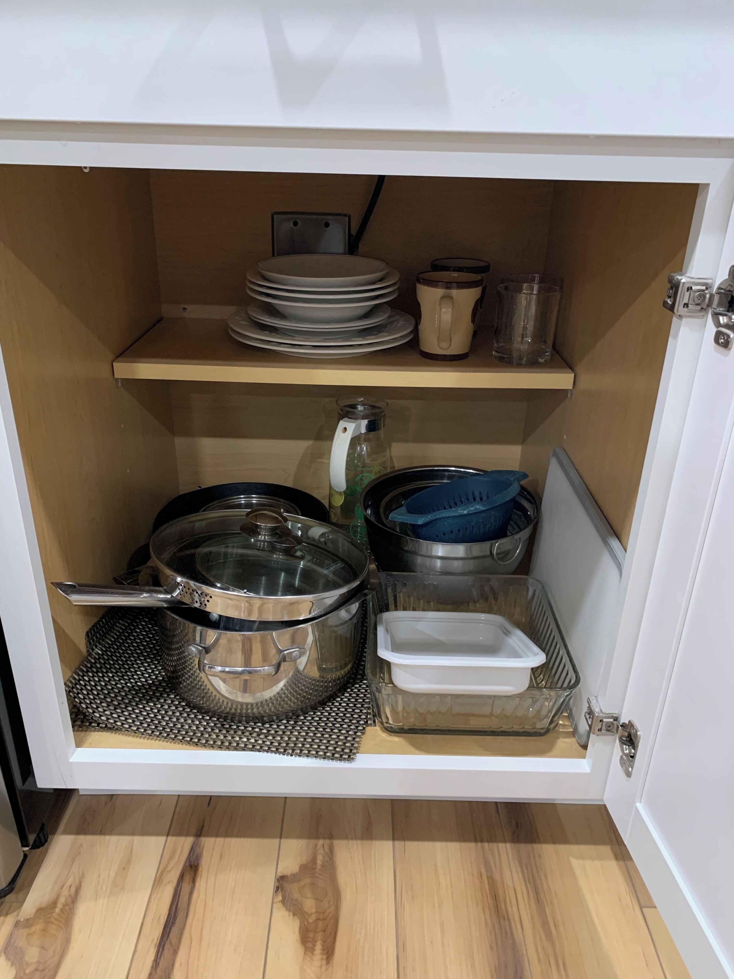 Um armário de cozinha com prateleiras que contêm louças, uma chaleira, panelas e um recipiente para alimentos.