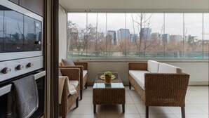 Uma sala de estar moderna com uma janela grande, móveis de vime, uma mesa de centro de vidro e um fogão embutido.