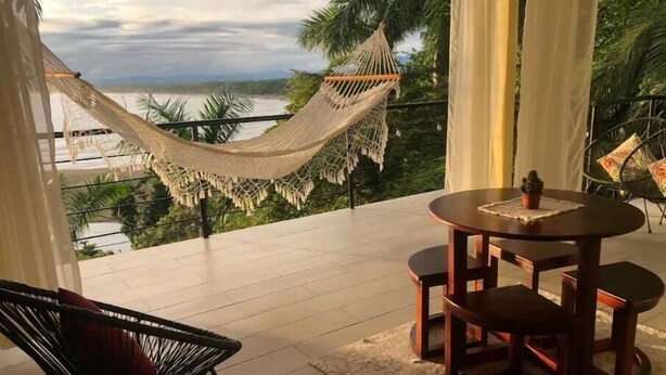 A balcony with a hammock, a round table with chairs, and a view of a body of water. - Ocean Sounds Private Apt for couples! Marina view (QUEPOS)