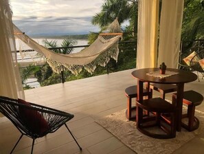 A balcony with a hammock, a round table with chairs, and a view of a body of water. - Ocean Sounds Private Apt for couples! Marina view (QUEPOS)