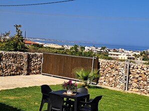 A patio with a table and chairs, a potted plant, and a view of the sea and buildings.