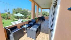 A covered outdoor seating area with wicker furniture, a table with a mat, and a green umbrella.
