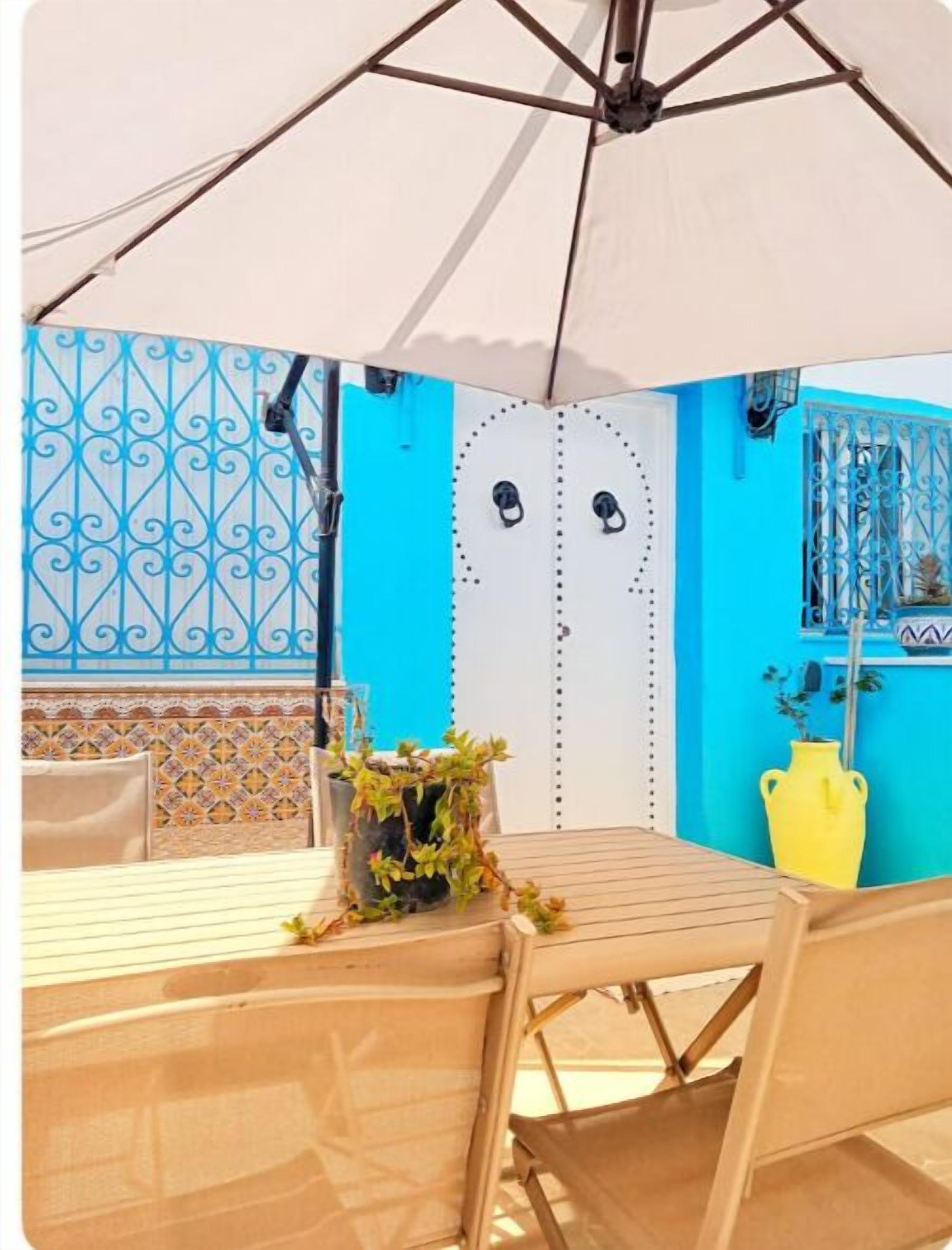 A room with a white umbrella, a table, chairs, and a blue wall with decorative patterns.