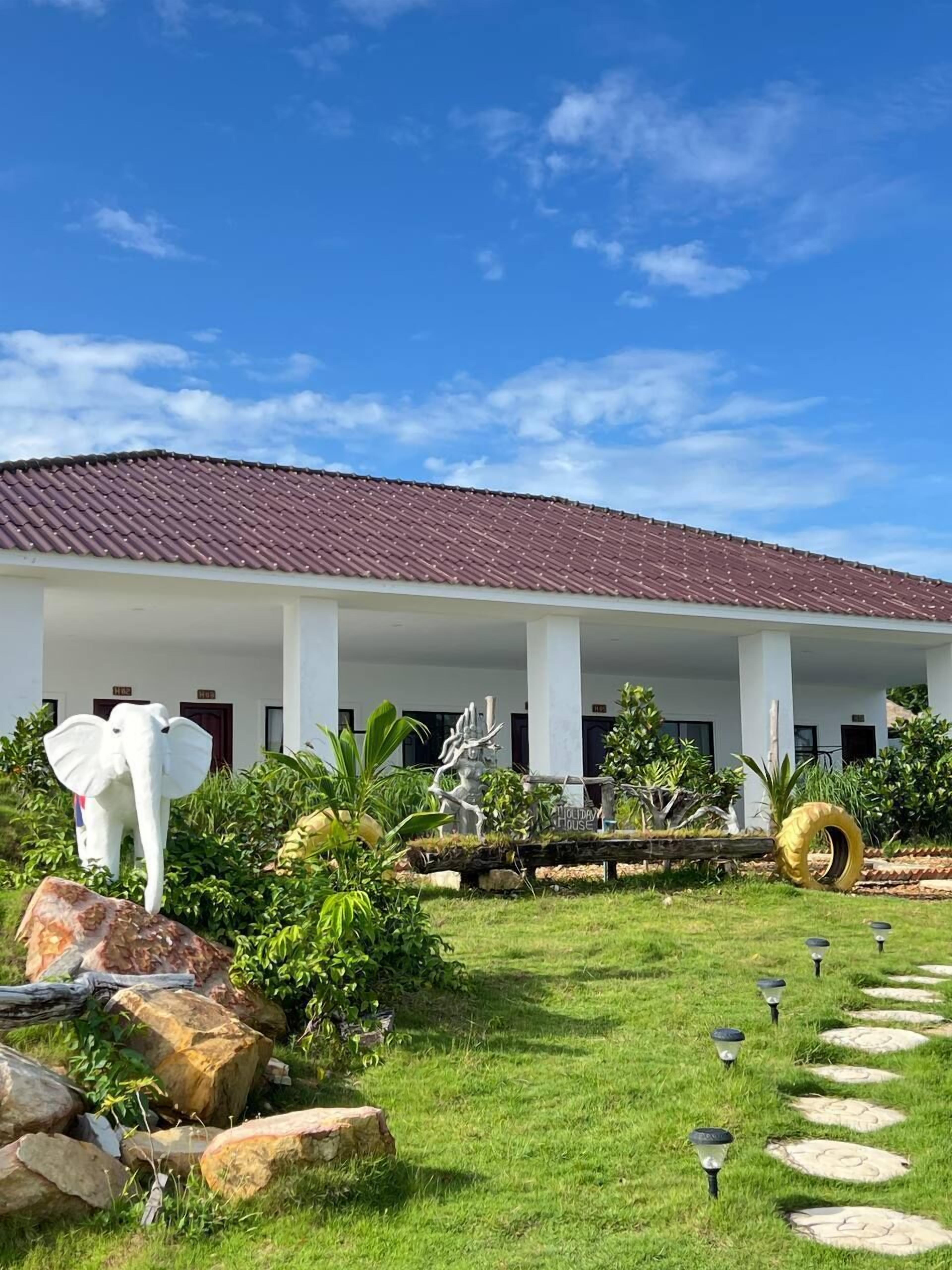 A building with a red-tiled roof, white columns, and a well-maintained lawn with decorative sculptures and stepping stones.