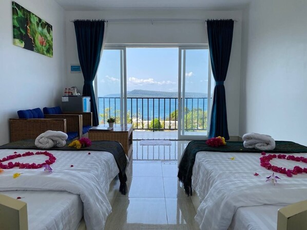 A hotel room with two beds, a balcony, and a view of the sea.