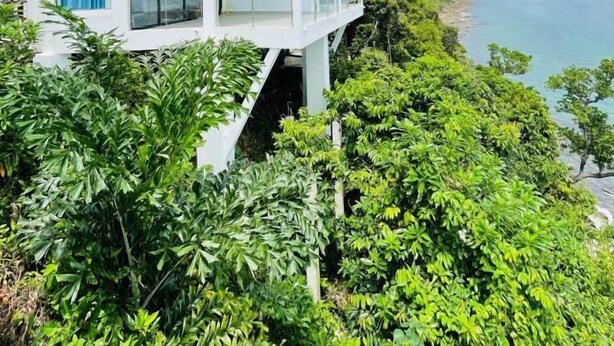 Una casa blanca con balcón que da a un paisaje verde exuberante y un cuerpo de agua.