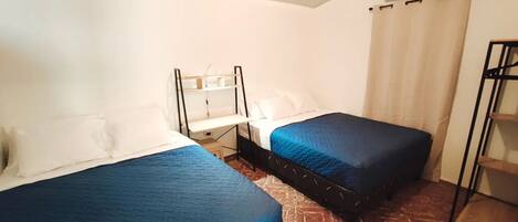 A small, compact room with two single beds, a bedside table, and a shelf unit.