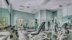 Een sportschool met diverse fitnessapparaten, grote ramen en een spiegel aan de muur.