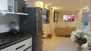 A modern kitchen with a refrigerator, microwave, and blender. There is a dining area with a table and chairs, and a television mounted on the wall. - Recanto da Sulla, Seu Refúgio Perfeito: Piscina Privativa, Área Gourmet e Charme (Jauá Camaçari)