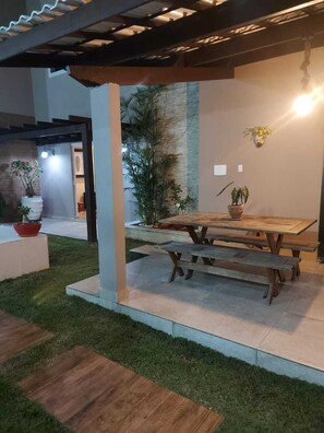An outdoor patio area with a wooden table and benches, surrounded by potted plants and a stone wall.