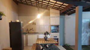 An outdoor kitchen area with a wooden table and benches, a refrigerator, and a pizza oven. - Recanto da Sulla, Seu Refúgio Perfeito: Piscina Privativa, Área Gourmet e Charme (Jauá Camaçari)