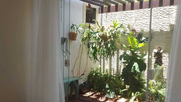 A room with a sliding glass door leading to a garden area with potted plants and a stone pathway. - Recanto da Sulla, Seu Refúgio Perfeito: Piscina Privativa, Área Gourmet e Charme (Jauá Camaçari)