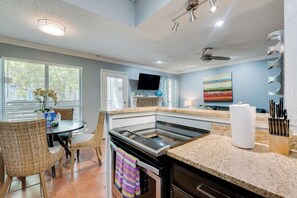 A modern kitchen with a built-in oven, a dining area with wicker chairs, and a large window with blinds.