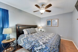 A bedroom with a bed, a nightstand, a lamp, a ceiling fan, and two framed pictures on the wall.