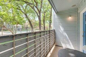 A balcony with a view of a swimming pool and trees, a blue door, and a small table.