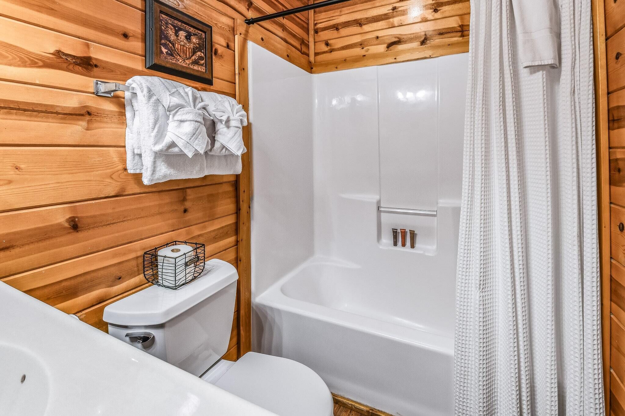 Une salle de bain avec des murs en bois, des toilettes blanches, une baignoire et un rideau de douche.