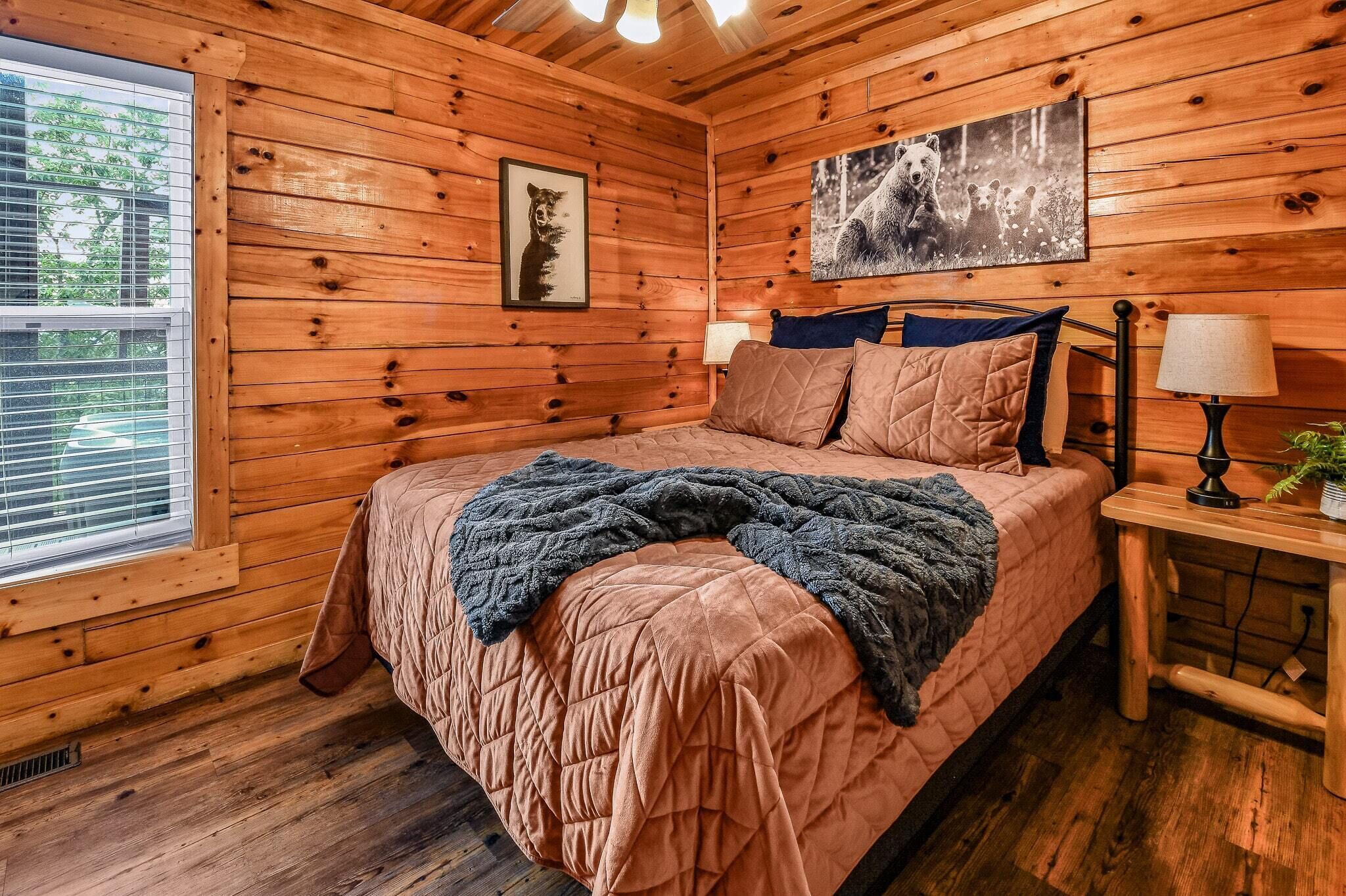 Une chambre dans un chalet en bois, avec un lit, deux lampes fixées au mur et une fenêtre avec des stores.