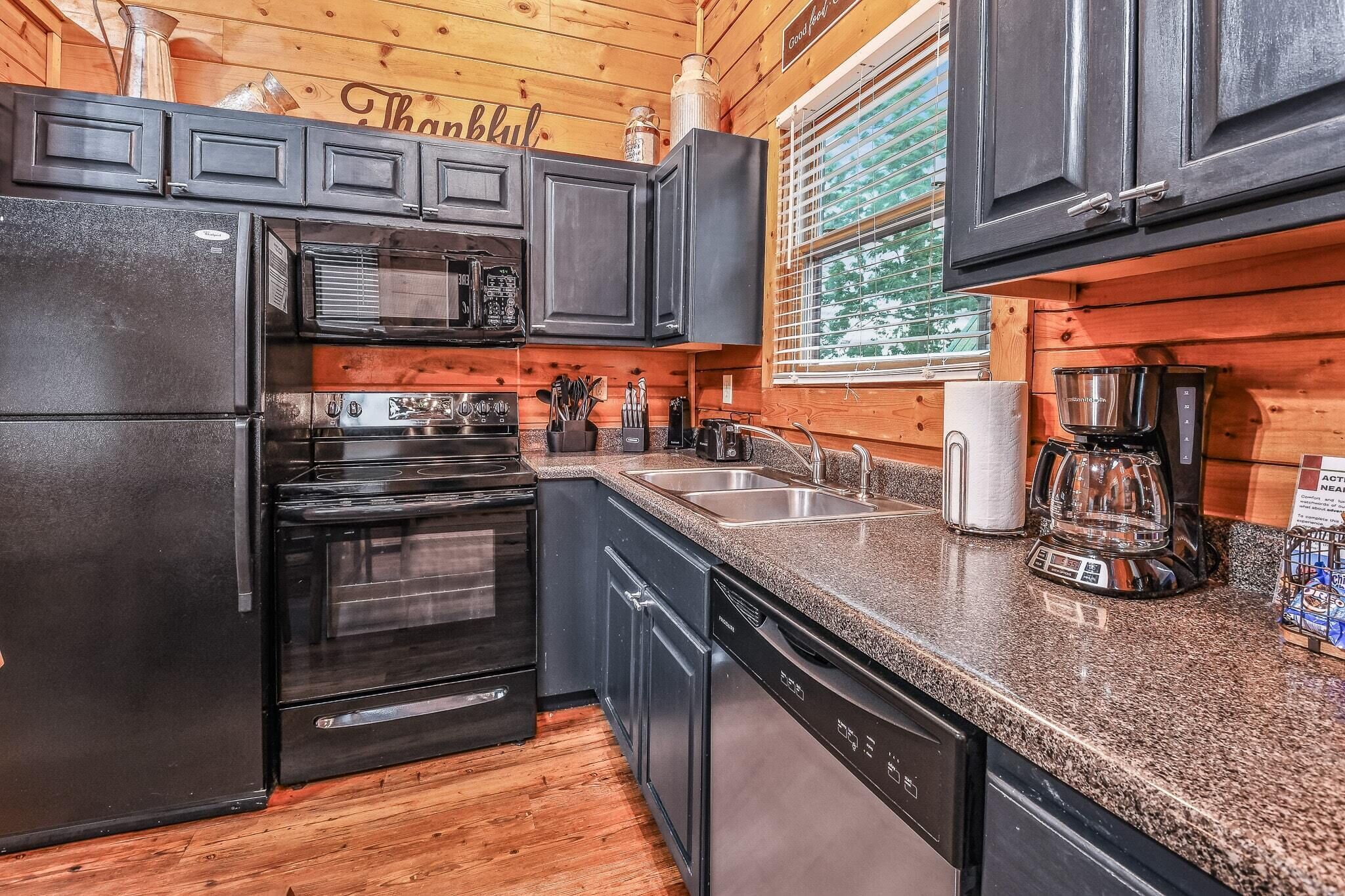 A modern kitchen with black appliances, granite countertops, and wooden walls.