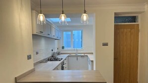 A modern kitchen with a central island, pendant lighting, and a view to the outside. - Charming Central Torquay Cottage (Torquay)