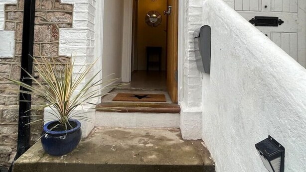 A staircase leading to a door with a stone wall on one side and a white wall on the other. - Charming Central Torquay Cottage (Torquay)